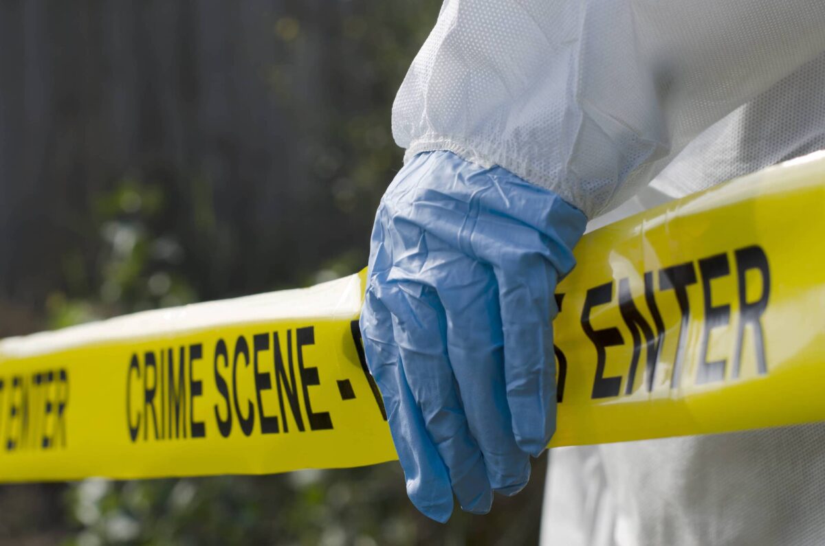 crime scene tape with a blue gloved cleaner's hand over it.